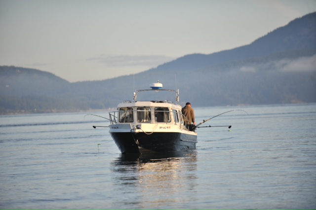 Highliner Charters' 26-foot Harbercraft Kingfisher fishing boat, viewed from another boat, with downriggers deployed and fishing poles attached, trolling in the water.